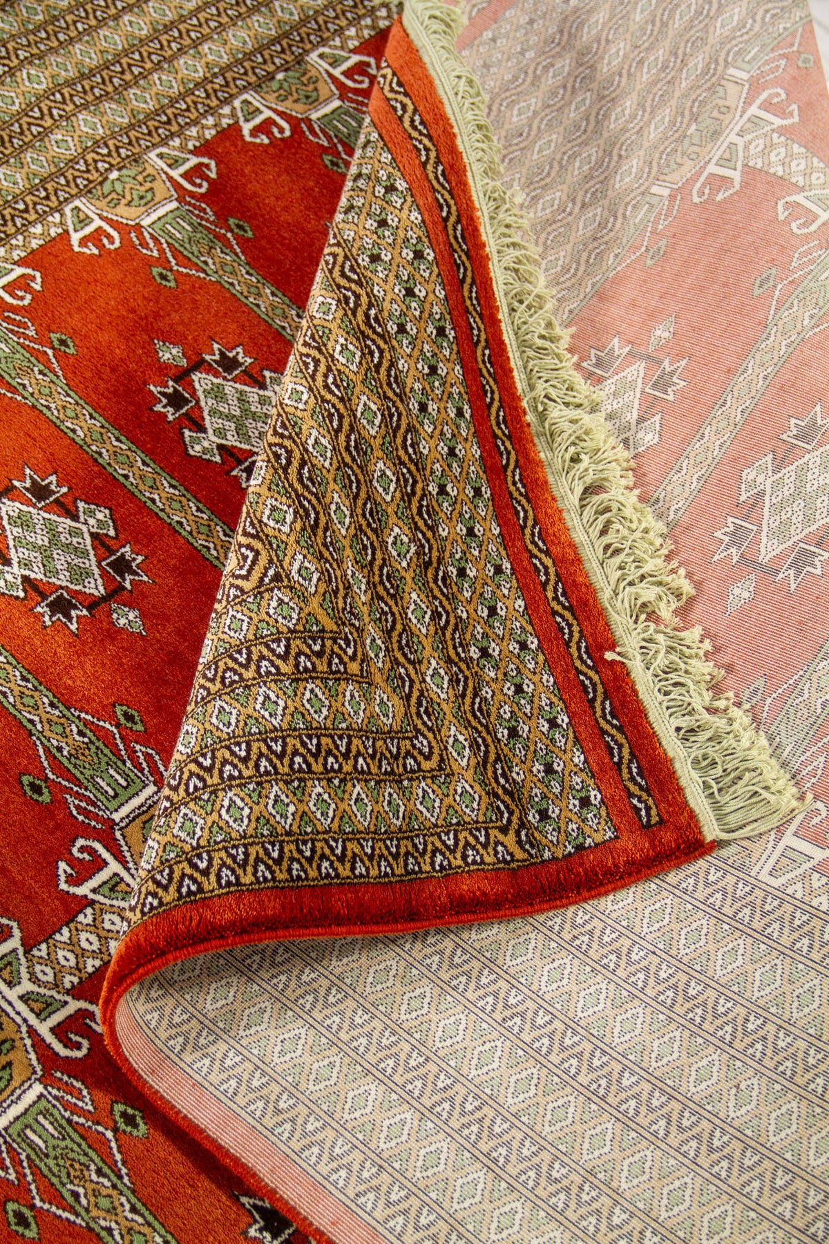 Detalle de alfombra doblada mostrando el frente rojo con motivos geométricos y el reverso del tejido con diseño visible.