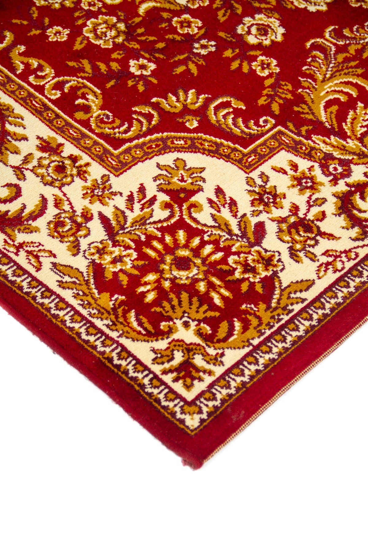 Primer plano de borde y esquina de alfombra clásica en tonos rojo, blanco suave y dorado, con motivos florales curvos y acabado prolijo.