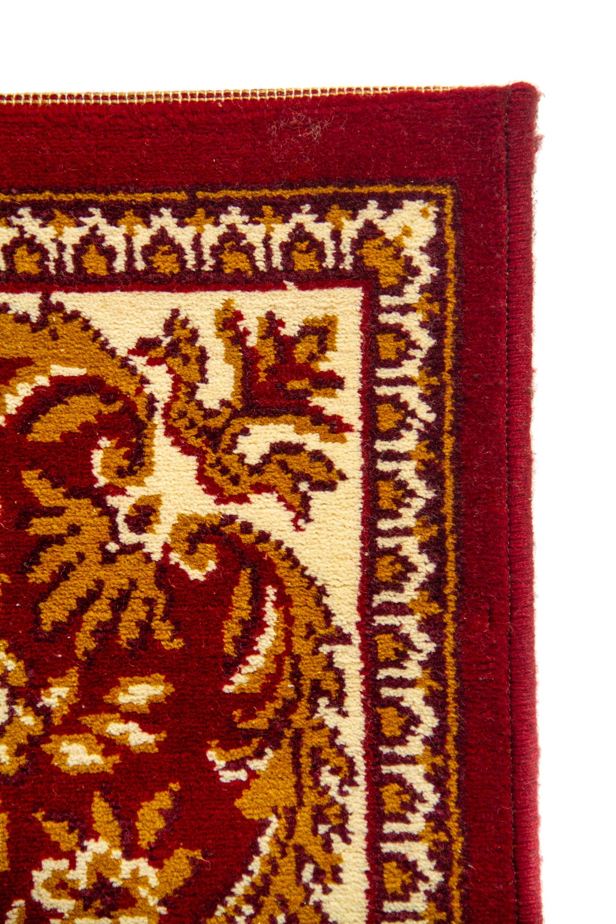 Detalle de esquina de alfombra roja con marco exterior liso, guarda ornamental delgada y decoración floral en tonos cálidos.