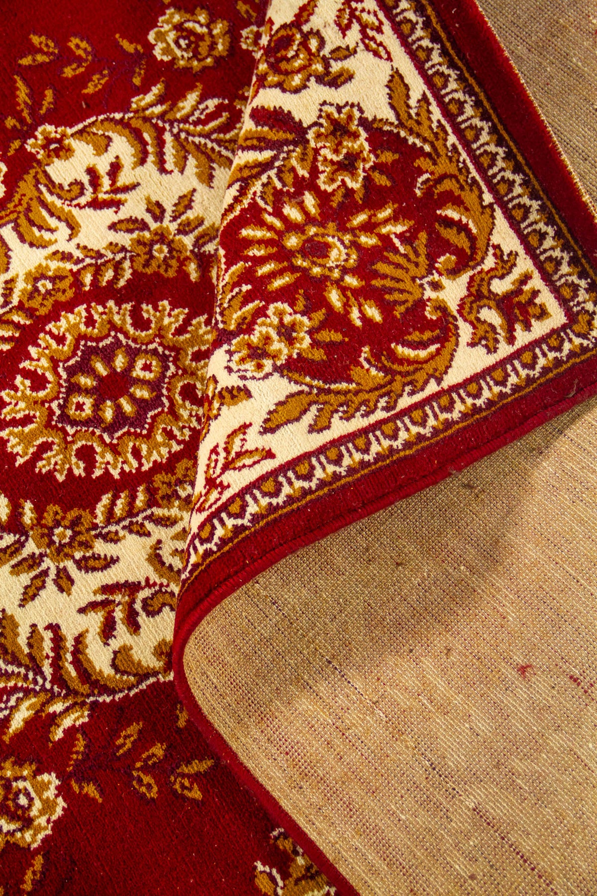 Alfombra doblada mostrando el reverso del tejido y un acercamiento a los motivos florales en rojo, blanco suave y dorado