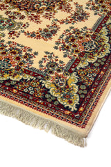 Detalle de esquina de alfombra clásica con fondo blanco suave, motivos florales minuciosos, guarda azul oscuro y roja, y flecos claros en el borde inferior