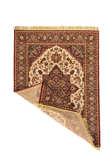 Alfombra clásica de fondo beige con una esquina doblada que muestra el reverso, medallón central ornamentado y borde decorativo en tonos rojo, negro y beige.