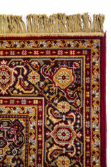 Acercamiento del extremo superior de la alfombra con flecos, mostrando el borde decorativo y la riqueza del tejido en tonos beige, rojo, negro y dorado.
