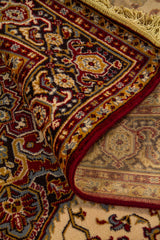 Detalle de alfombra doblada con vista del reverso, flecos y borde elaborado, destacando la textura del tejido y los motivos ornamentales del diseño central.