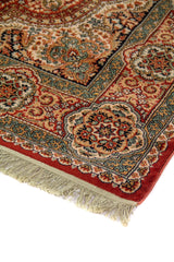 Detalle de esquina de alfombra oriental con flecos claros, guarda ancha de rosetones y arabescos, y centro en tonos rojo, blanco suave, azul suave y negro.