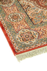 Primer plano del borde de una alfombra tradicional con cenefa ornamental, medallones circulares repetidos y finos motivos florales en tonos cálidos y azulados.