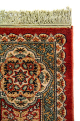 Acercamiento del extremo superior de la alfombra con flecos, mostrando la textura del tejido y los detalles del borde en rojo, blanco suave, azul suave y negro.