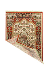 Alfombra tradicional en rojo y blanco suave con una esquina doblada que deja ver el reverso, los flecos color blanco suave y el detalle del borde decorativo.