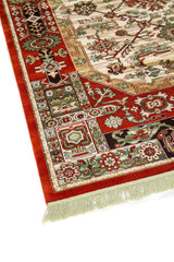 Detalle de esquina de alfombra clásica con fondo rojo intenso, guarda floral y geométrica multicolor, y flecos color blanco suave.