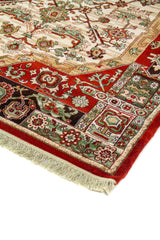 Acercamiento del borde y campo central de alfombra de estilo tradicional con motivos geométricos y florales en rojo, beige, verde y negro.