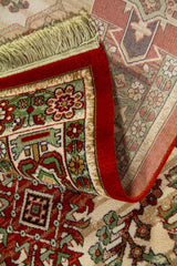 Detalle de alfombra doblada mostrando el reverso tejido, el canto rojo aterciopelado y los flecos color blanco suave.