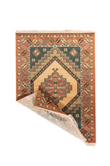 Alfombra clásica de inspiración geométrica con una esquina doblada que deja ver el reverso tejido, el borde decorativo y los flecos color blanco suave.