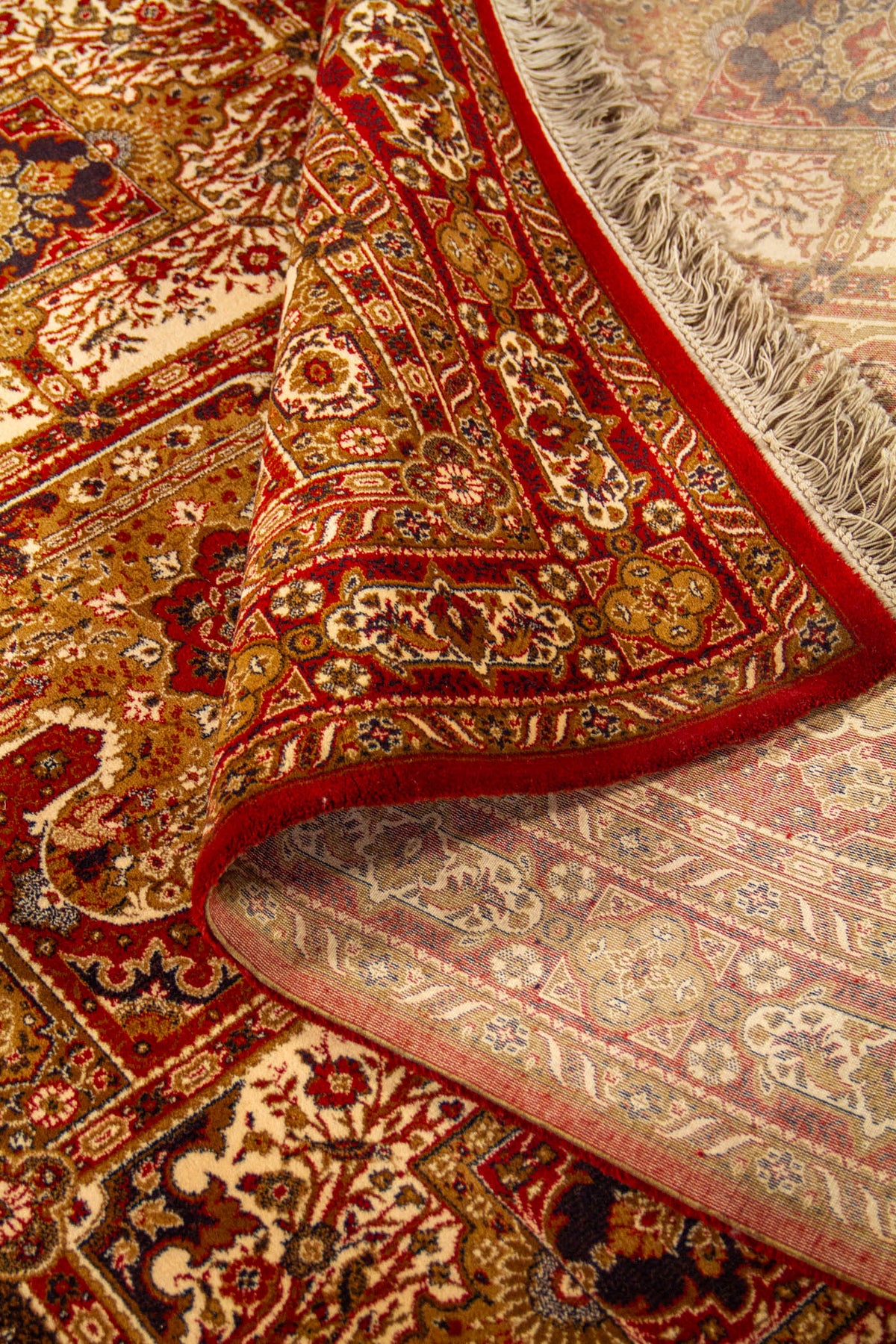 Detalle de alfombra oriental parcialmente doblada que deja ver el reverso, la textura del tejido, los flecos y el diseño ornamental del borde.