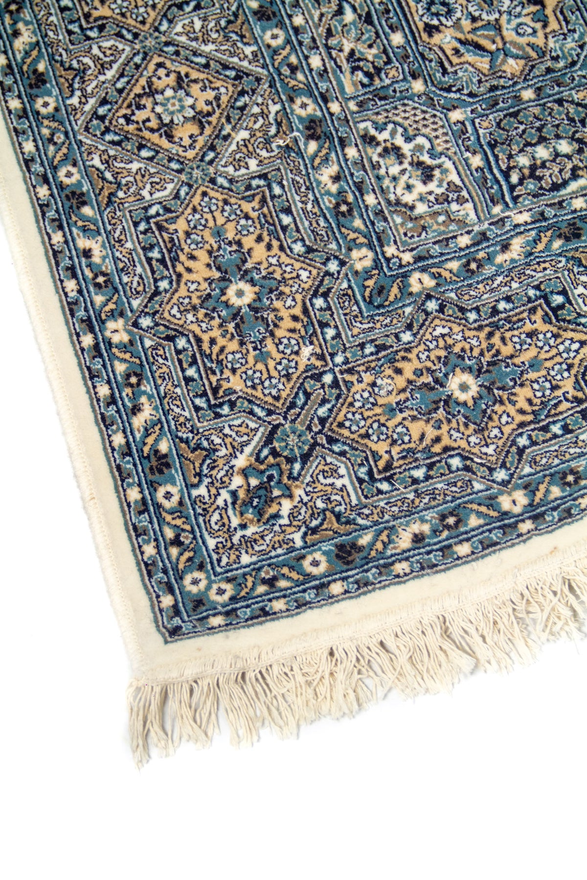 Detalle de esquina de alfombra oriental azul con flecos claros y motivos florales geométricos