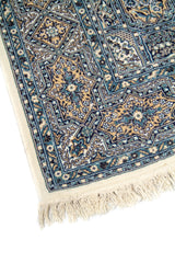 Detalle de esquina de alfombra oriental azul con flecos claros y motivos florales geométricos