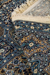 La alfombra aparece parcialmente doblada, mostrando su textura, el acabado del tejido y la definición de los dibujos. Esta toma enfatiza la riqueza visual de los paneles interiores y la calidad ornamental del conjunto.