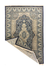 Alfombra azul y beige con esquina doblada que muestra el reverso, los flecos y el diseño central decorativo