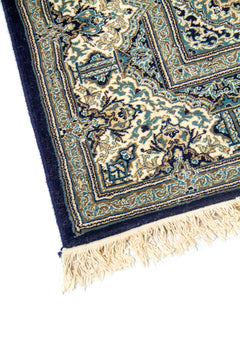 Acercamiento de borde de alfombra azul oscuro y beige con guarda floral y ornamentos simétricos