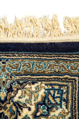 Detalle de flecos y borde superior de alfombra oriental azul con diseño floral en tonos blanco suave y celeste