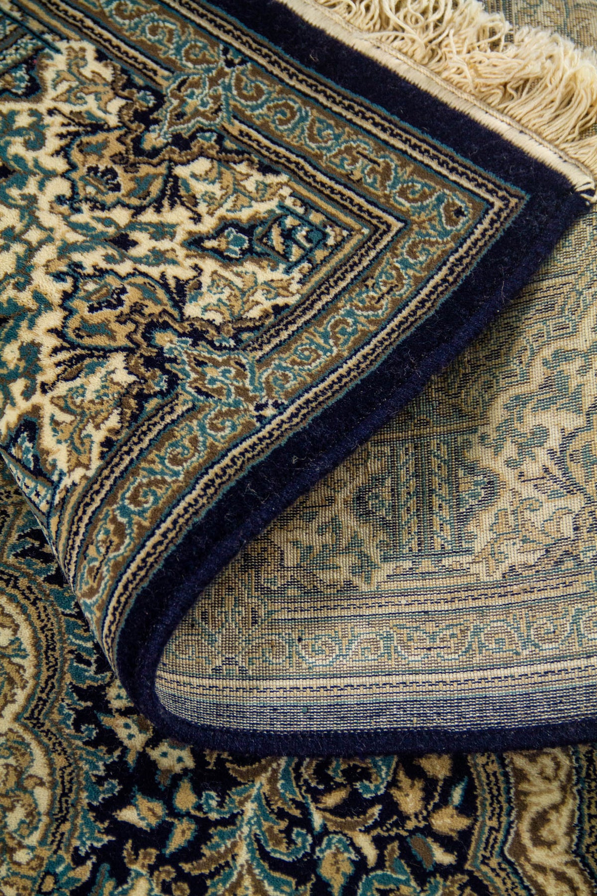 Alfombra doblada con reverso visible y detalle de cenefa azul, beige y blanco suave