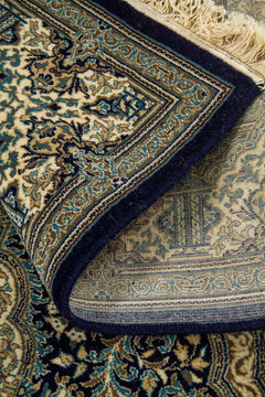 Alfombra doblada con reverso visible y detalle de cenefa azul, beige y blanco suave