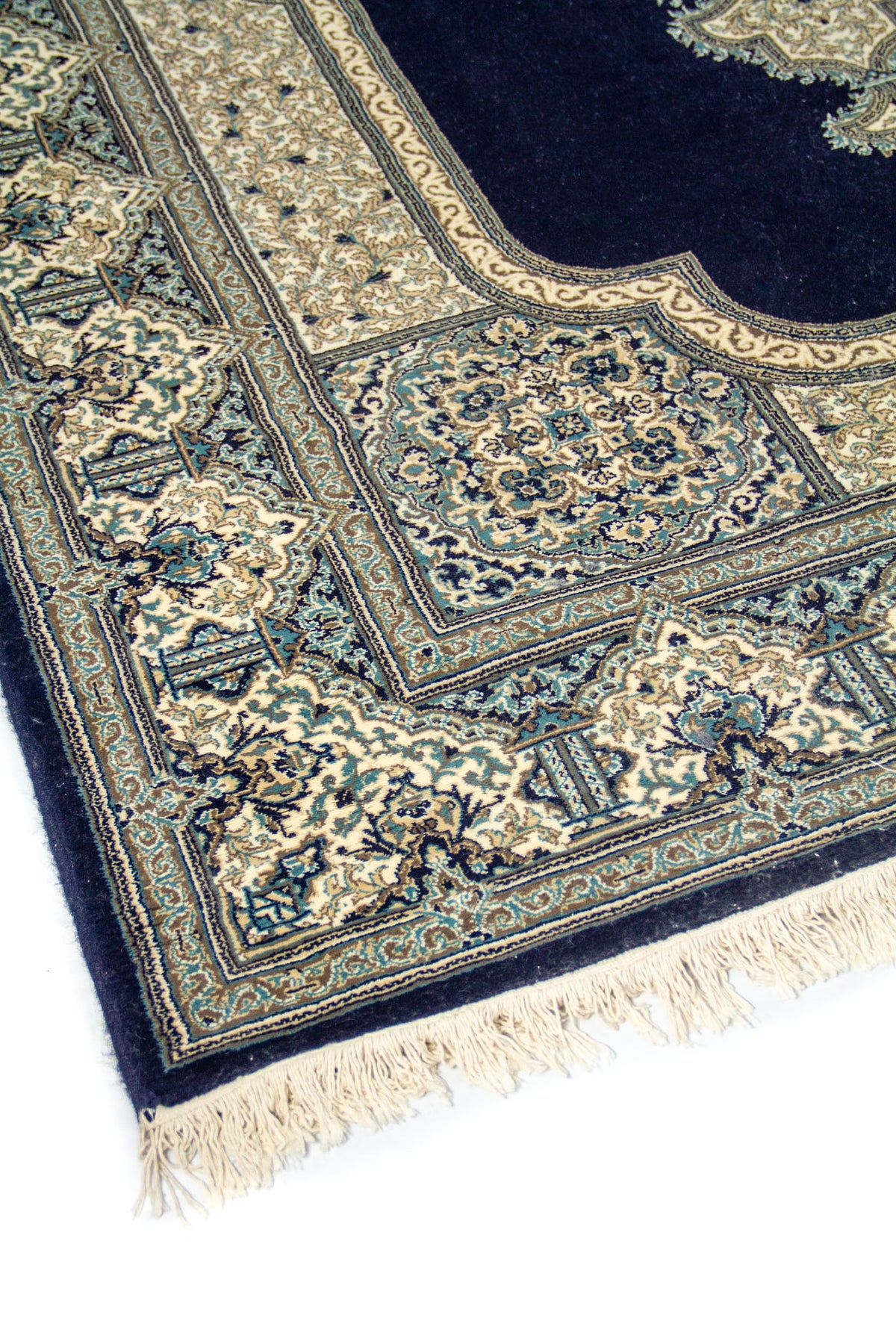 Primer plano de alfombra clásica azul oscuro y beige con motivos florales, marcos decorativos y acabado con flecos claros.