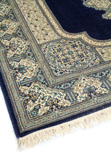 Primer plano de alfombra clásica azul oscuro y beige con motivos florales, marcos decorativos y acabado con flecos claros.