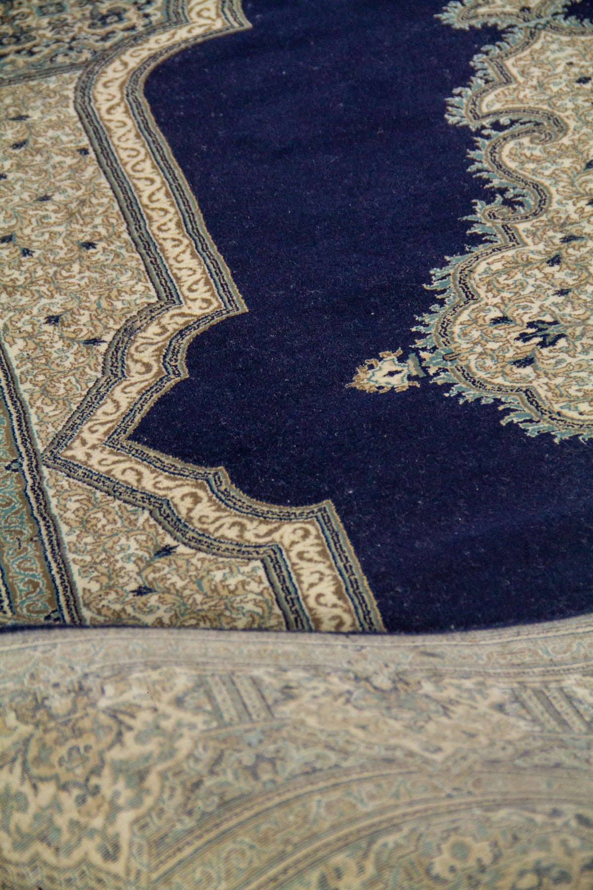 Detalle cercano del campo central azul oscuro de la alfombra, con borde interno blanco suave y patrones ornamentales finamente trabajados.