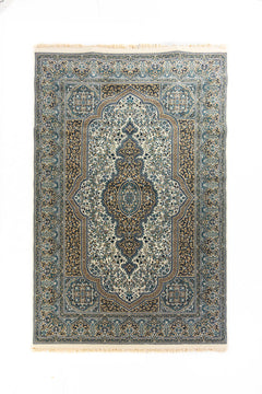 Alfombra clásica rectangular en tonos blanco suave, azul y beige con gran medallón central, arabescos florales y guardas ornamentales.