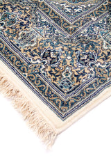 Detalle de esquina de alfombra con flecos color blanco suave, borde ornamental y delicados motivos florales en tonos azul y beige.
