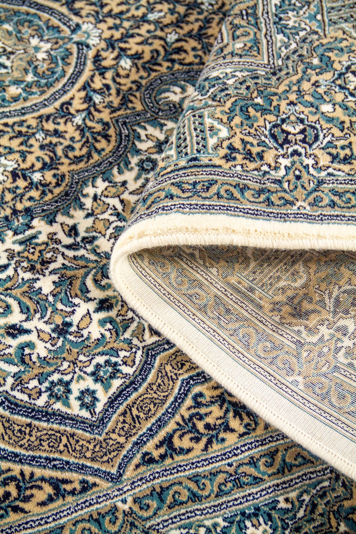 Alfombra parcialmente enrollada que muestra la textura, el reverso tejido y el diseño ornamental floral en tonos blanco suave, azul y beige.