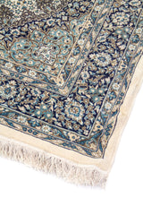 Detalle de esquina de alfombra clásica con guarda floral azul, fondo blanco suave y flecos claros en uno de sus extremos