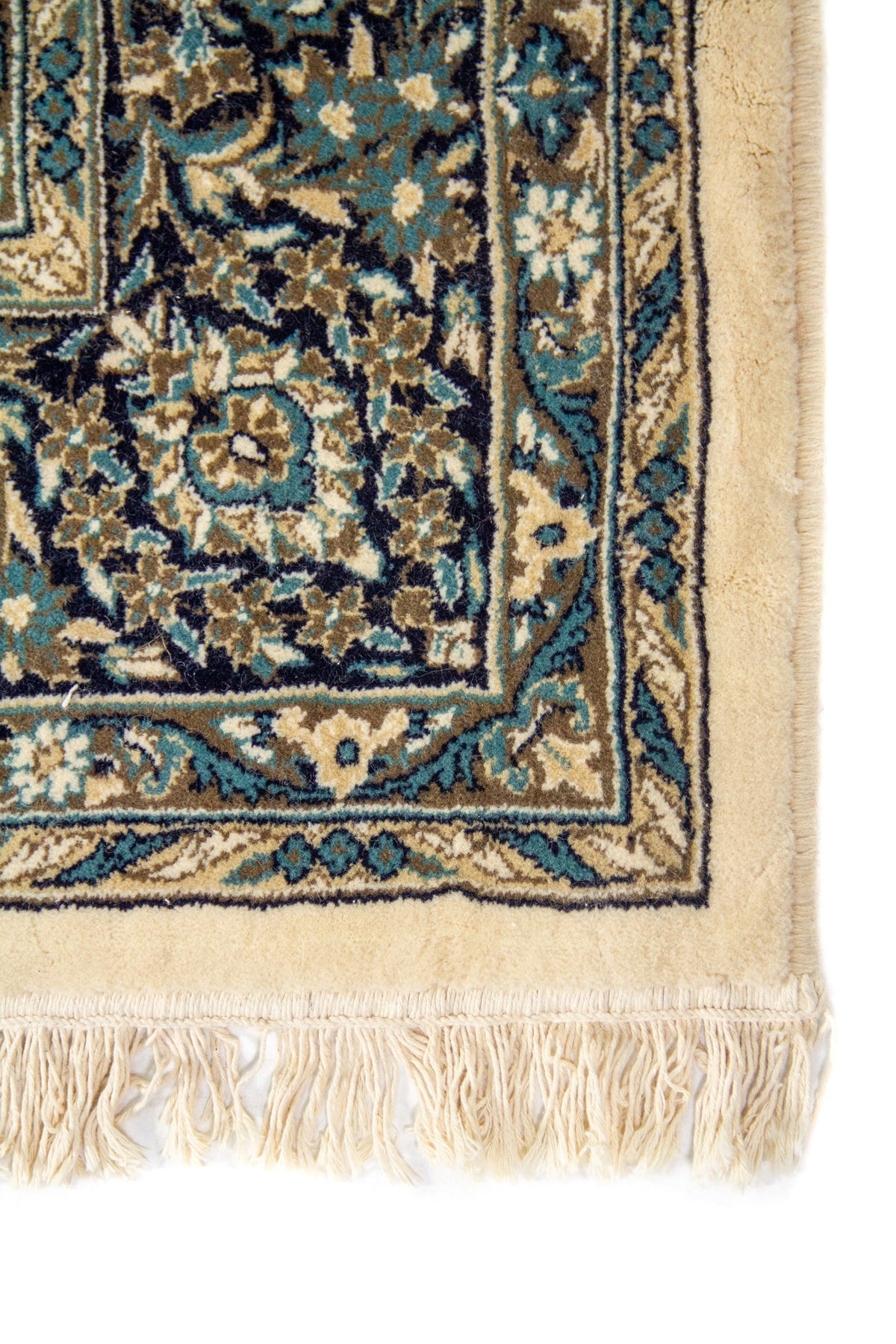 Primer plano de esquina de alfombra ornamental en tonos blanco suave, azul y gris, con borde definido y motivos florales minuciosos.