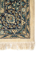 Primer plano de esquina de alfombra ornamental en tonos blanco suave, azul y gris, con borde definido y motivos florales minuciosos.