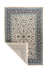 Alfombra oriental en tonos blanco suave y azul con una esquina doblada que deja ver el reverso, los flecos y el acabado del tejido.
