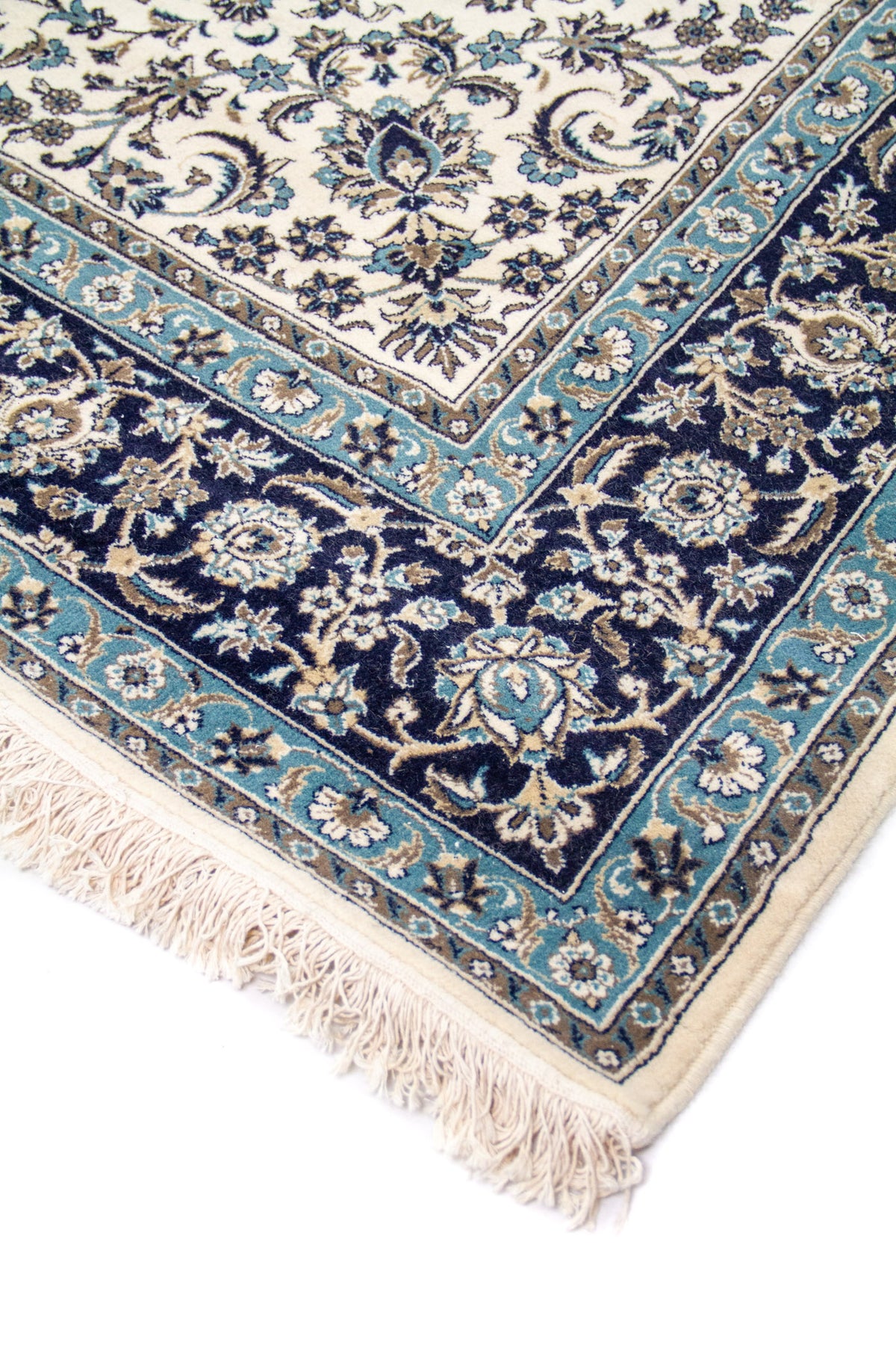 Detalle de esquina de alfombra clásica con fondo blanco suave, guarda azul oscuro y celeste, motivos florales y flecos claros