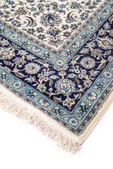 Detalle de esquina de alfombra clásica con fondo blanco suave, guarda azul oscuro y celeste, motivos florales y flecos claros