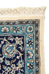 Primer plano de esquina de alfombra ornamental con borde blanco suave y diseño floral en tonos azul, celeste y beige