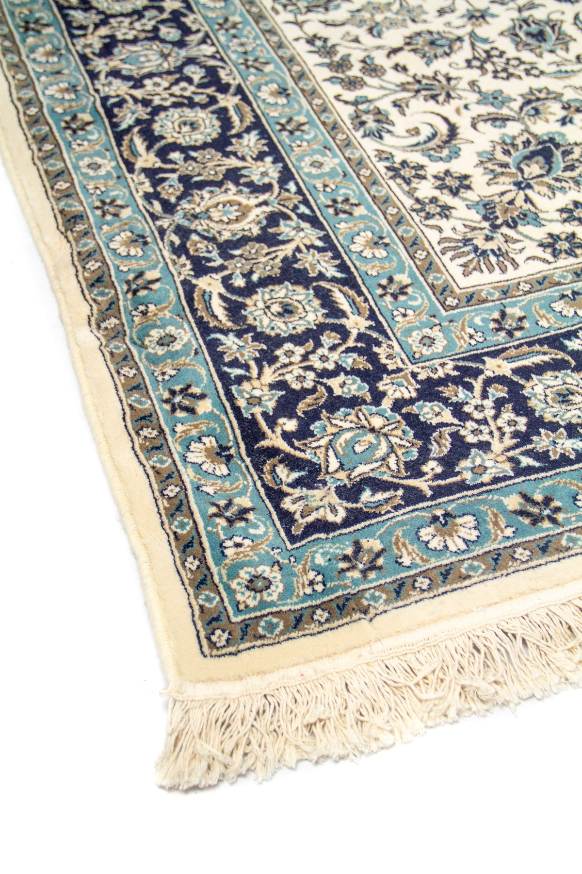 Vista en diagonal de la alfombra mostrando la guarda floral azul, el extremo con flecos y el contraste del fondo claro con los detalles oscuros.