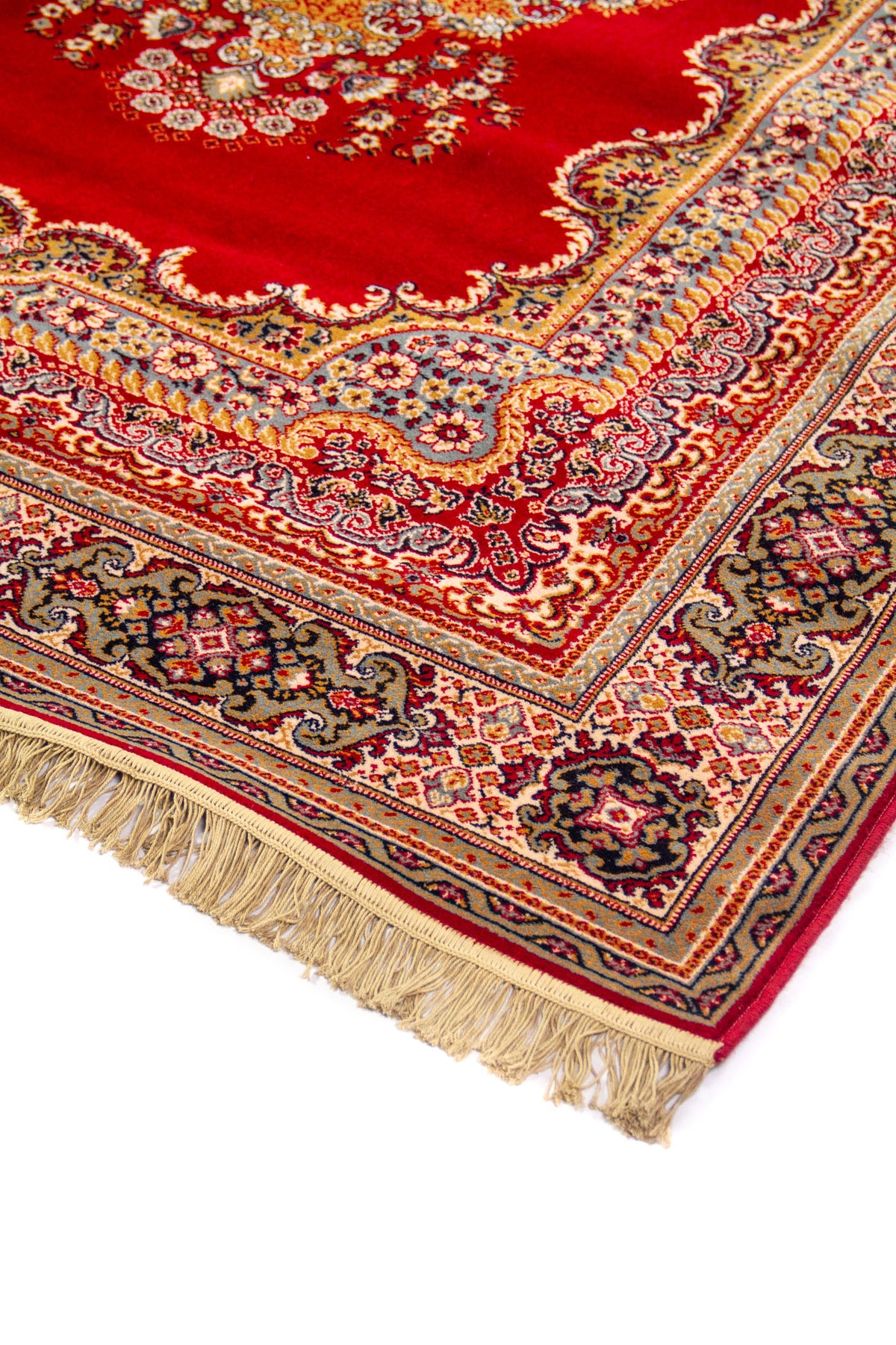 Detalle en perspectiva de alfombra clásica roja con diseño floral, borde ornamental en tonos beige y azul, y flecos claros en el extremo.