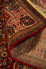 Detalle de alfombra oriental parcialmente doblada mostrando el reverso, la textura del tejido y la riqueza ornamental del borde.
