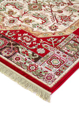 Detalle en perspectiva de alfombra clásica con borde rojo, motivos geométricos y florales en tonos blanco suave, verde y beige, y flecos en el extremo.