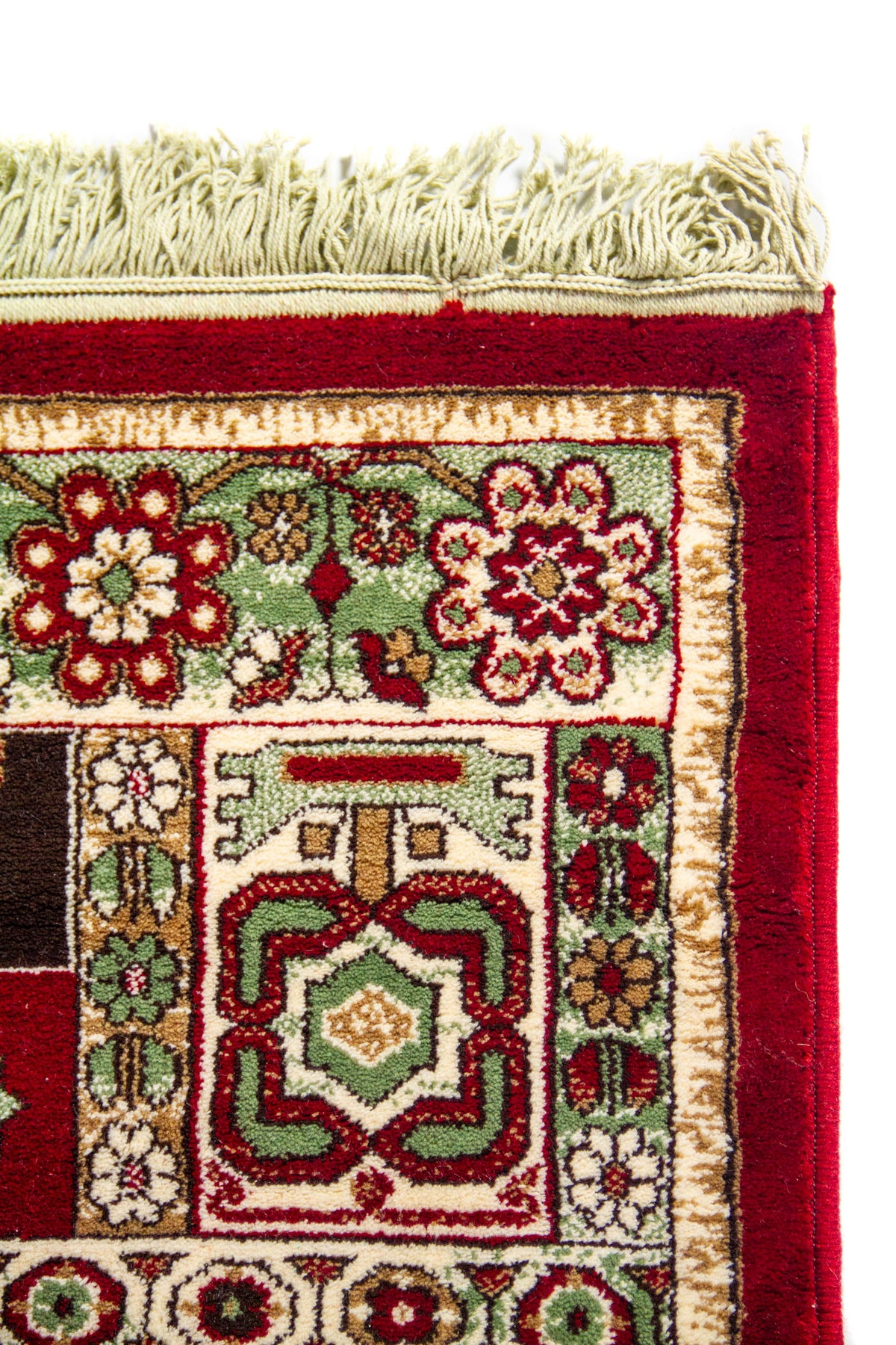 Primer plano de la esquina de una alfombra roja clásica con flecos claros, patrones florales geométricos y borde decorativo en tonos blanco suave y verde.