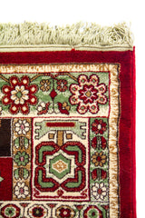 Primer plano de la esquina de una alfombra roja clásica con flecos claros, patrones florales geométricos y borde decorativo en tonos blanco suave y verde.