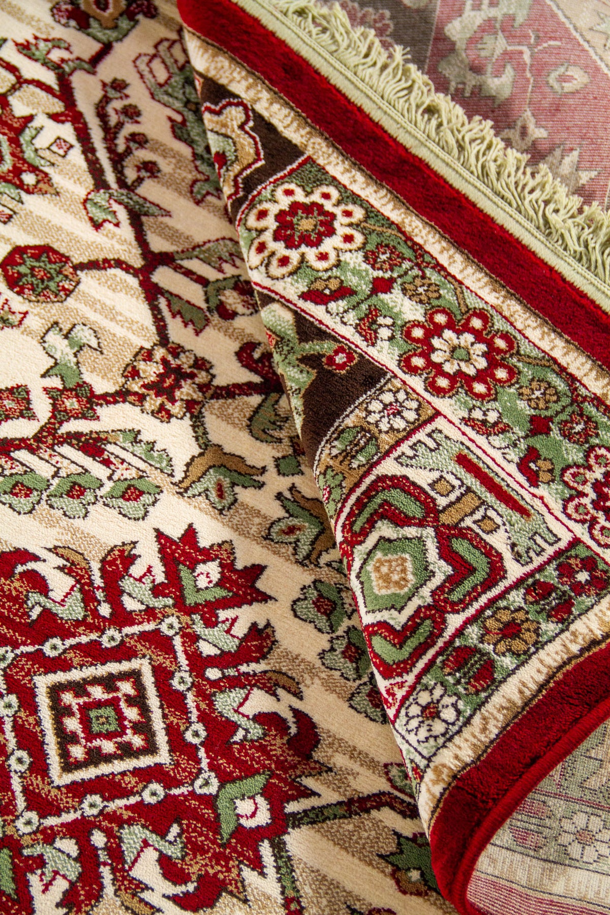 Detalle de alfombra oriental parcialmente doblada que deja ver el reverso, la textura del tejido y la riqueza ornamental del diseño geométrico.