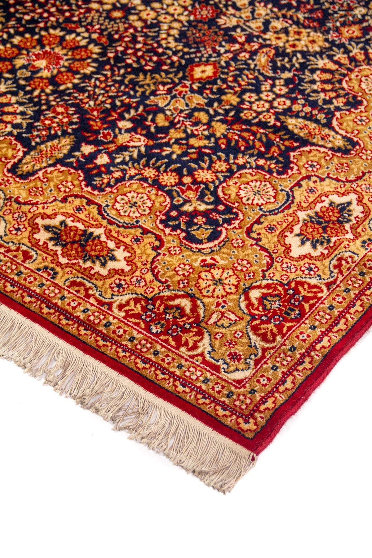 Detalle en perspectiva de alfombra clásica con fondo azul oscuro, motivos florales en tonos dorados y rojos, y flecos claros en el borde.