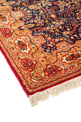 Acercamiento lateral de alfombra oriental floral con guarda dorada, detalles en rojo y beige, y terminación con flecos en el extremo.