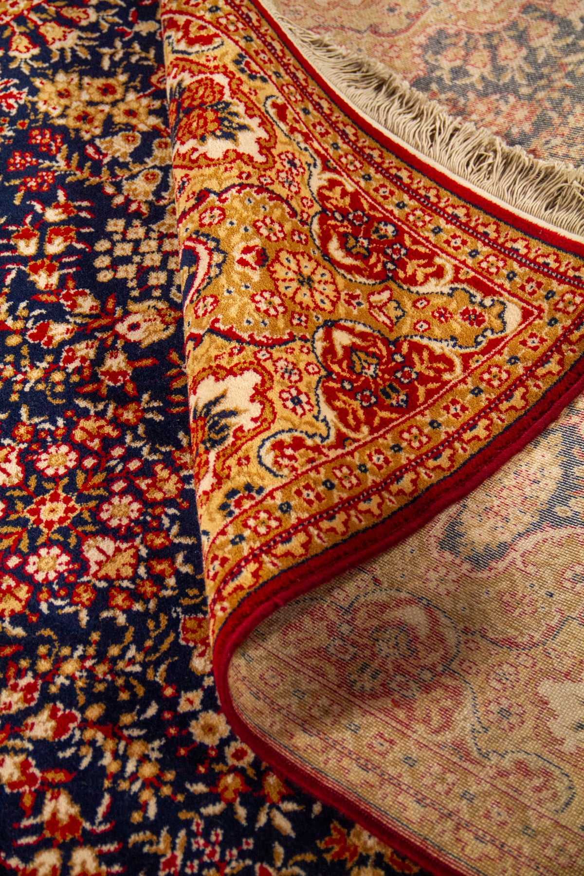 Detalle de alfombra oriental parcialmente doblada que deja ver el reverso, la textura del tejido y la riqueza del diseño floral del borde.