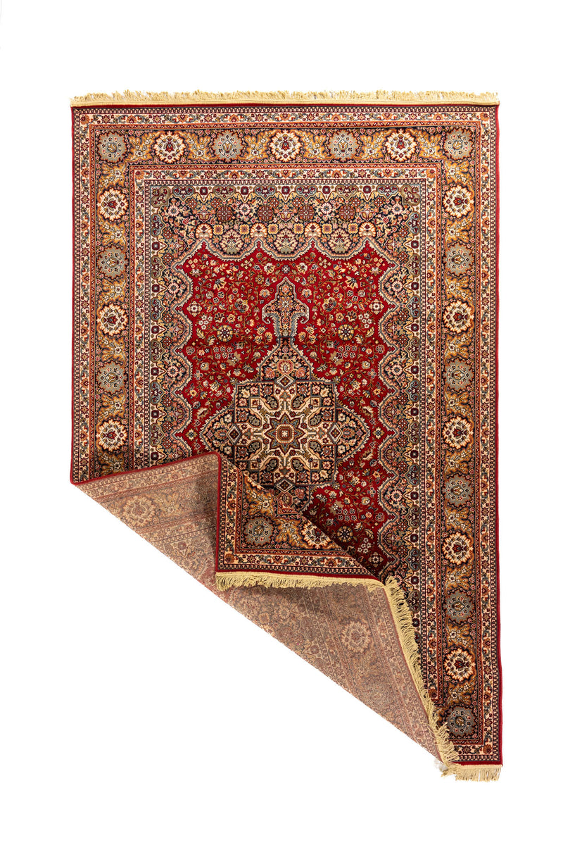 Alfombra oriental clásica con una esquina doblada que muestra el reverso, la estructura del tejido, los flecos beige y el borde decorativo.