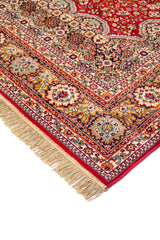Detalle en perspectiva de alfombra roja clásica con motivos florales, cenefa ornamental en tonos beige, azul y dorado, y flecos en el extremo.